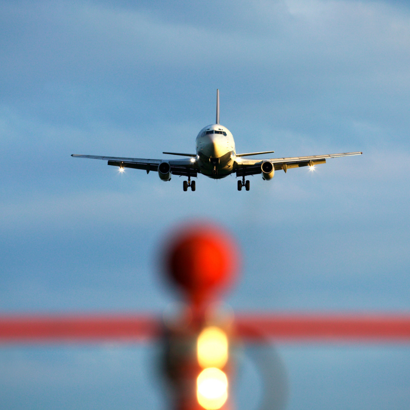 A commercial airplane on approach to land, viewed from the runway with approach lights in the foreground.